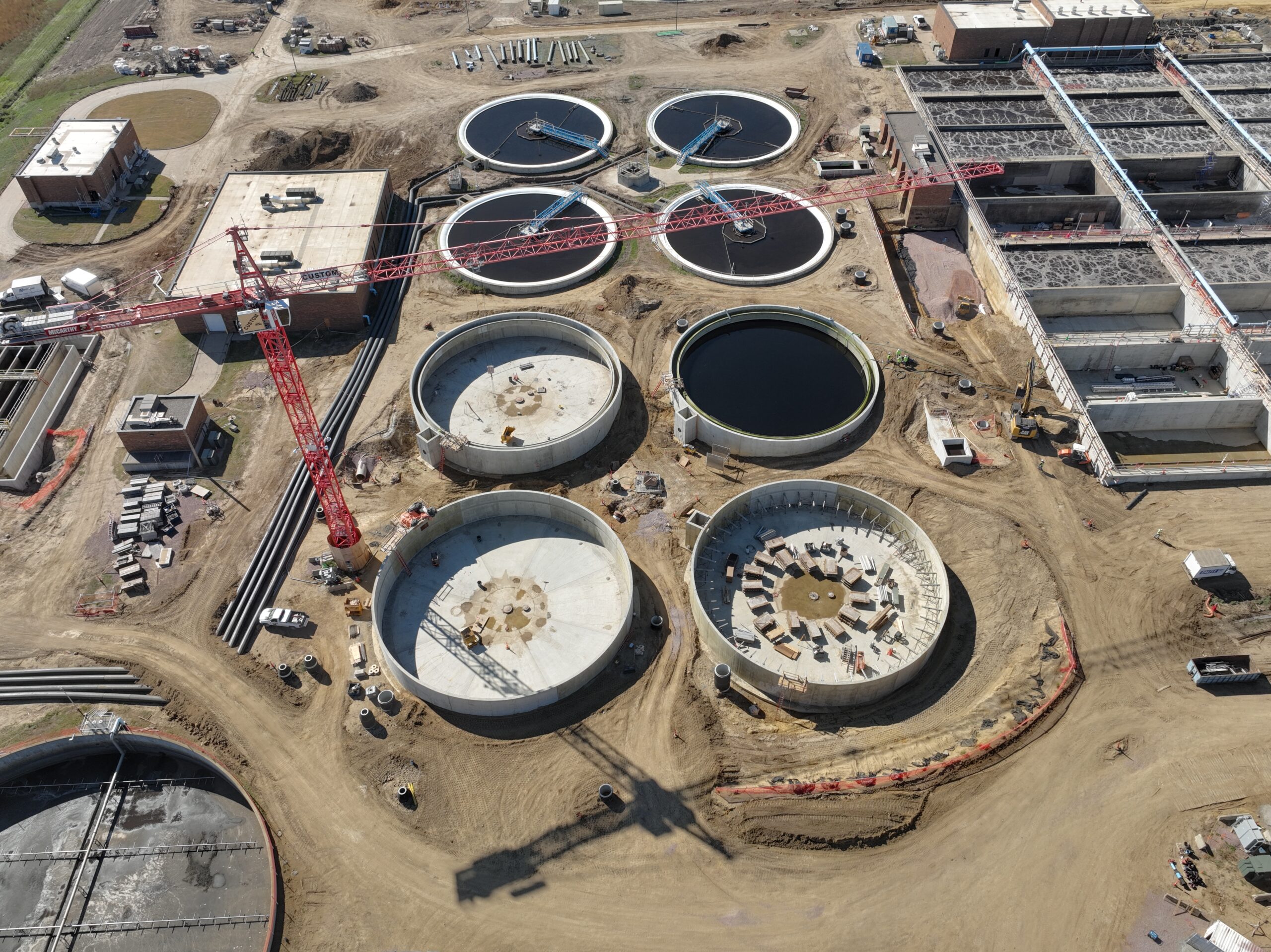 Aerial view of the City of Sioux Falls water reclamation plant project construction site with circular tanks and a red crane.