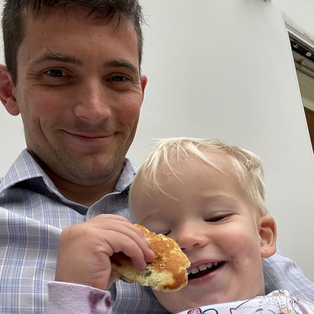 Father and child smiling. The child is holding a pastry and appears to be enjoying it.