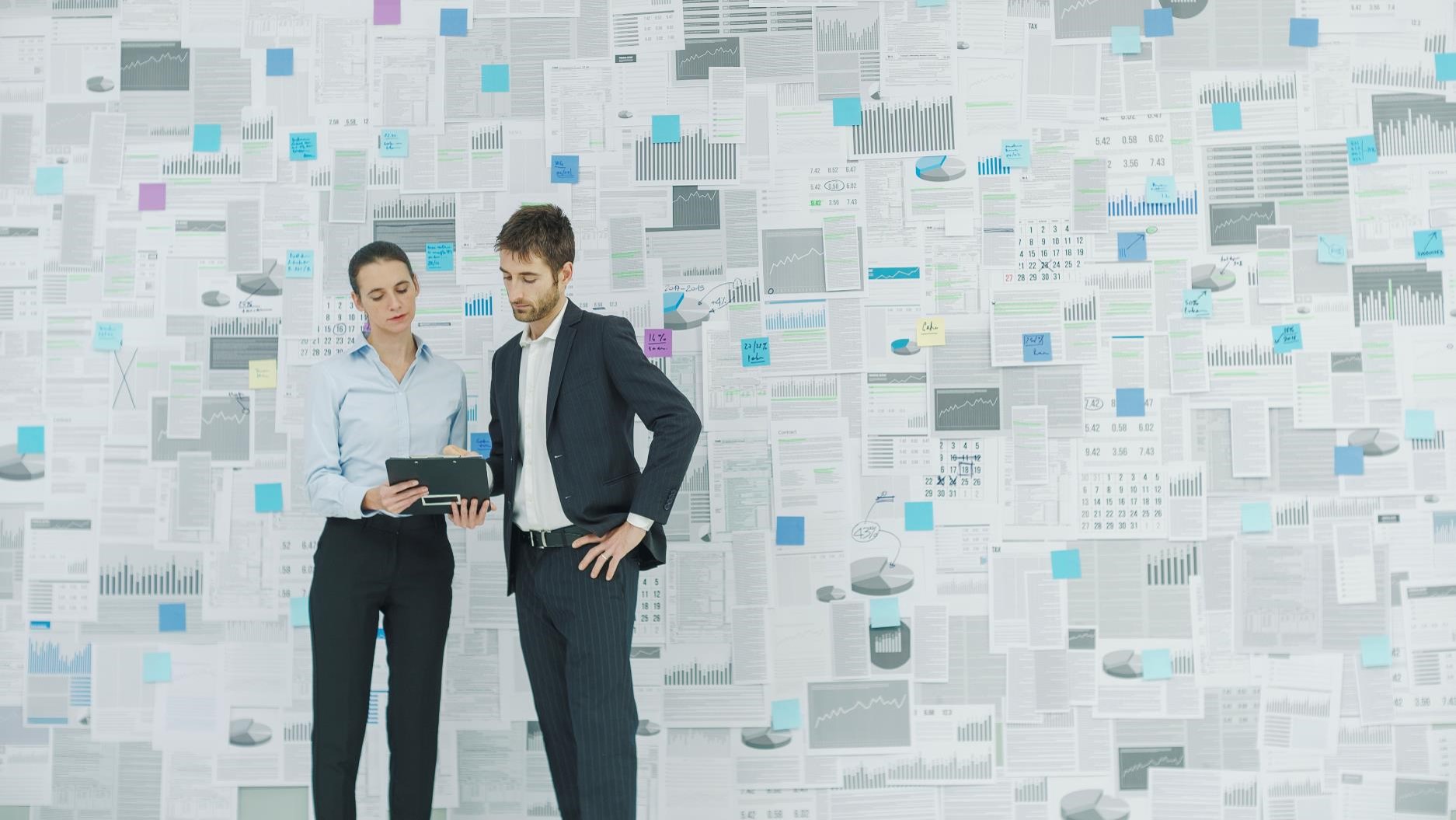 Business team analyzing data wall for tech investment value. Charts, graphs, and calendars displayed.