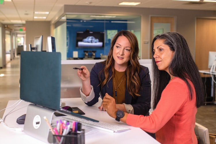 Two women collaborate at a computer in an office setting.