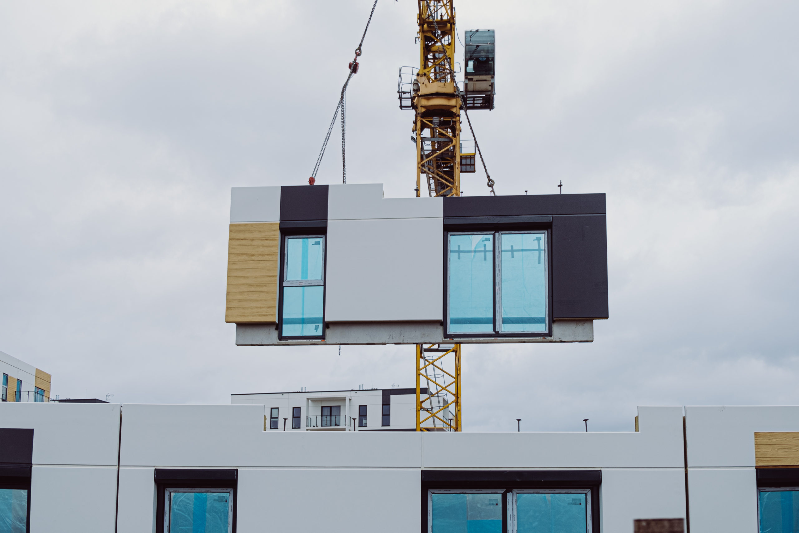 Prefabrication: Crane lifting a modular home unit into place at a construction site.