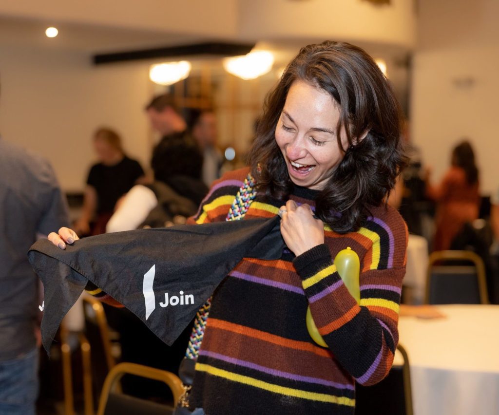 Enthusiastic woman holding a "Join" banner at a Company event, with a balloon in hand.