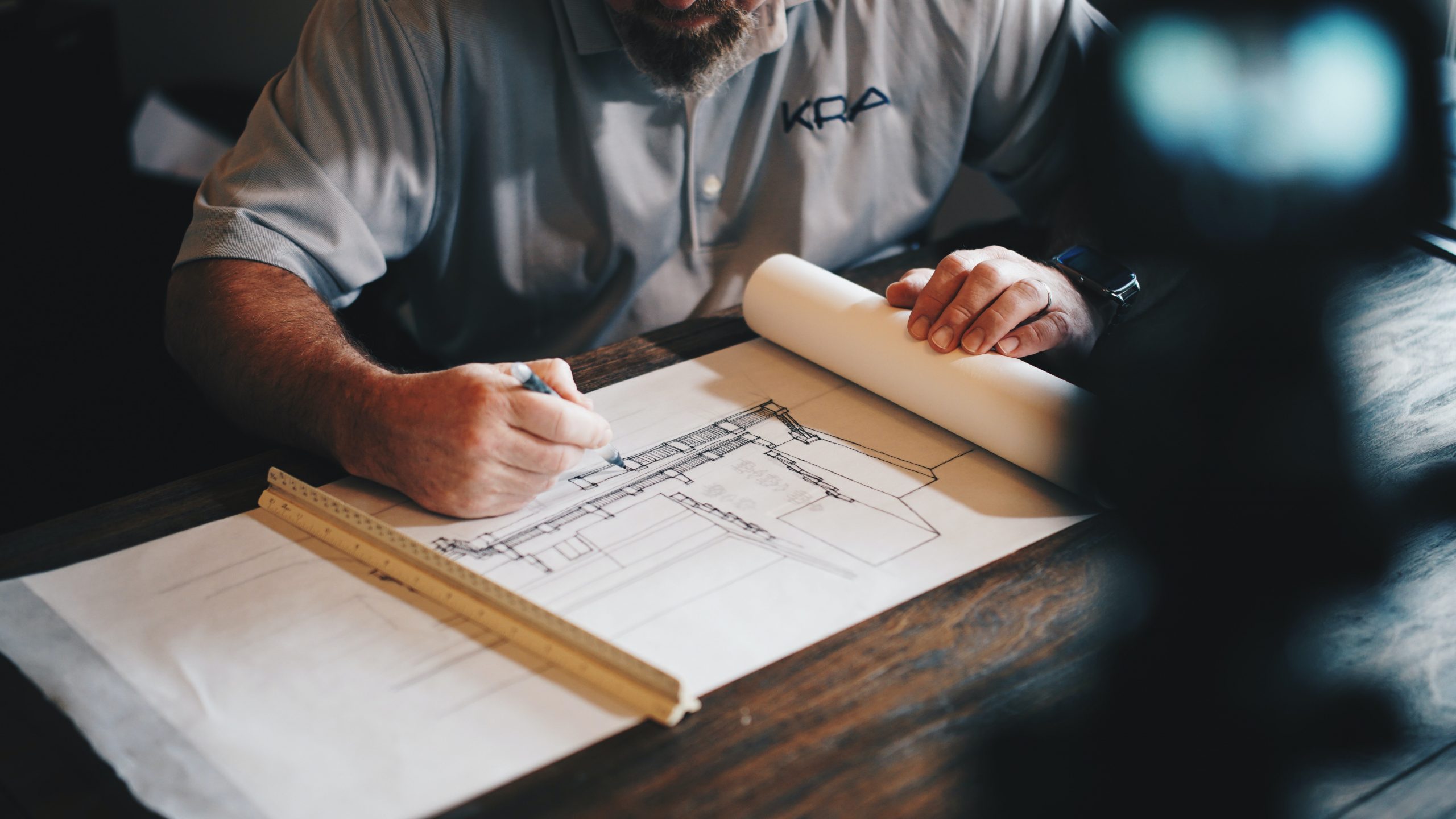 Architect drawing a preconstruction blueprint with a ruler on a wooden table.
