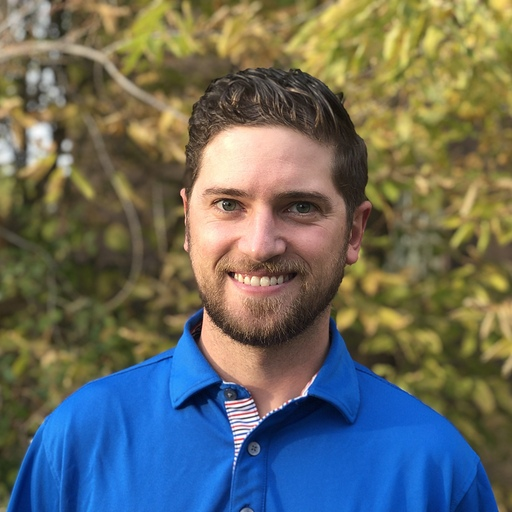 Smiling man in a blue polo shirt with a beard outdoors.