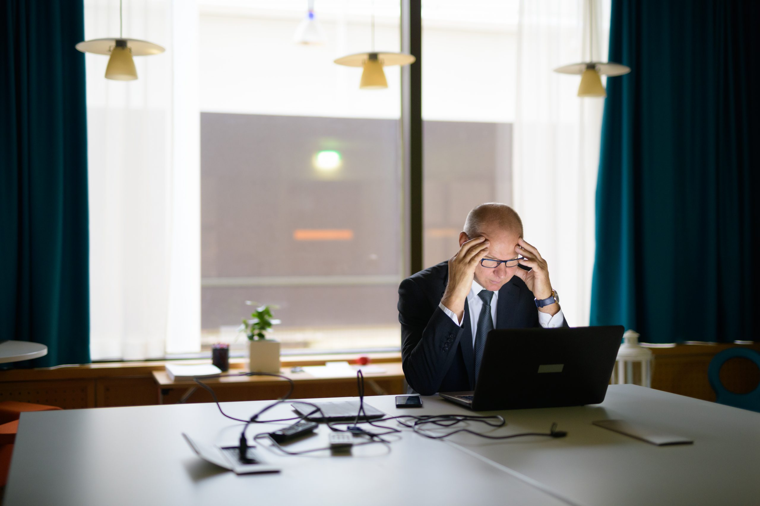 Stressed businessman at laptop, head in hands. Indecision costing you at work.
