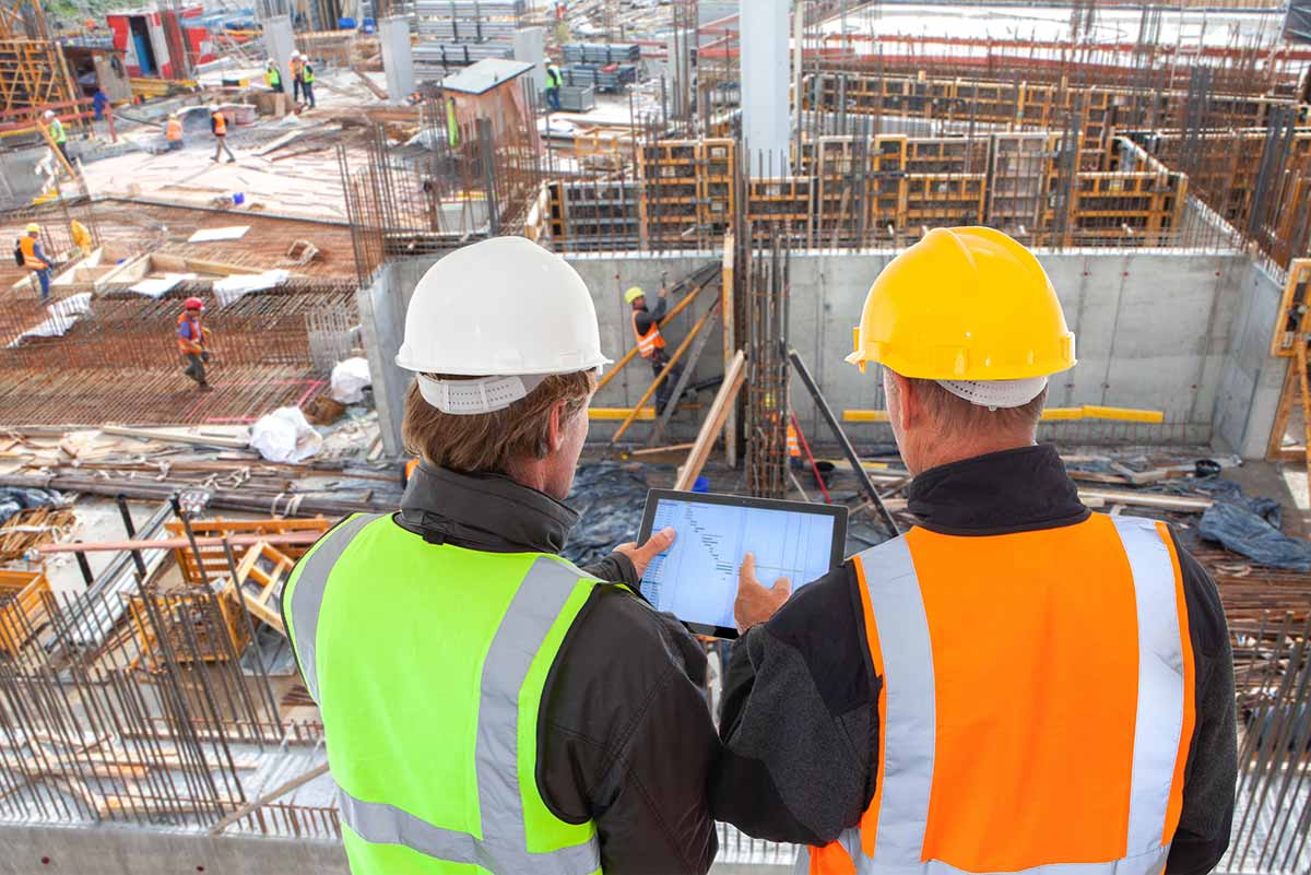 two engineers reviewing a project using construction management apps on their tablet|two engineers reviewing project plan on a tablet