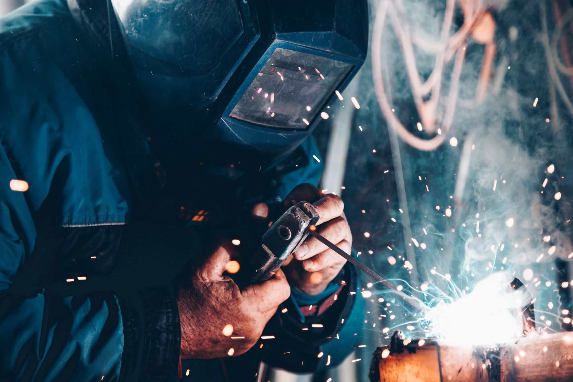 Welder wearing a mask, sparks flying. Building product manufacturing requires skilled labor.