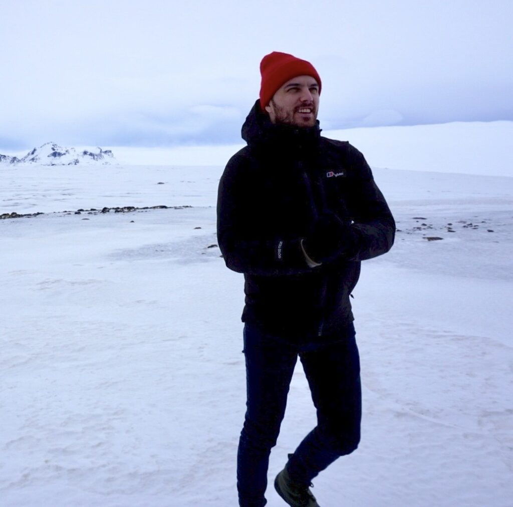 Man in red beanie and black jacket stands in a snowy landscape.