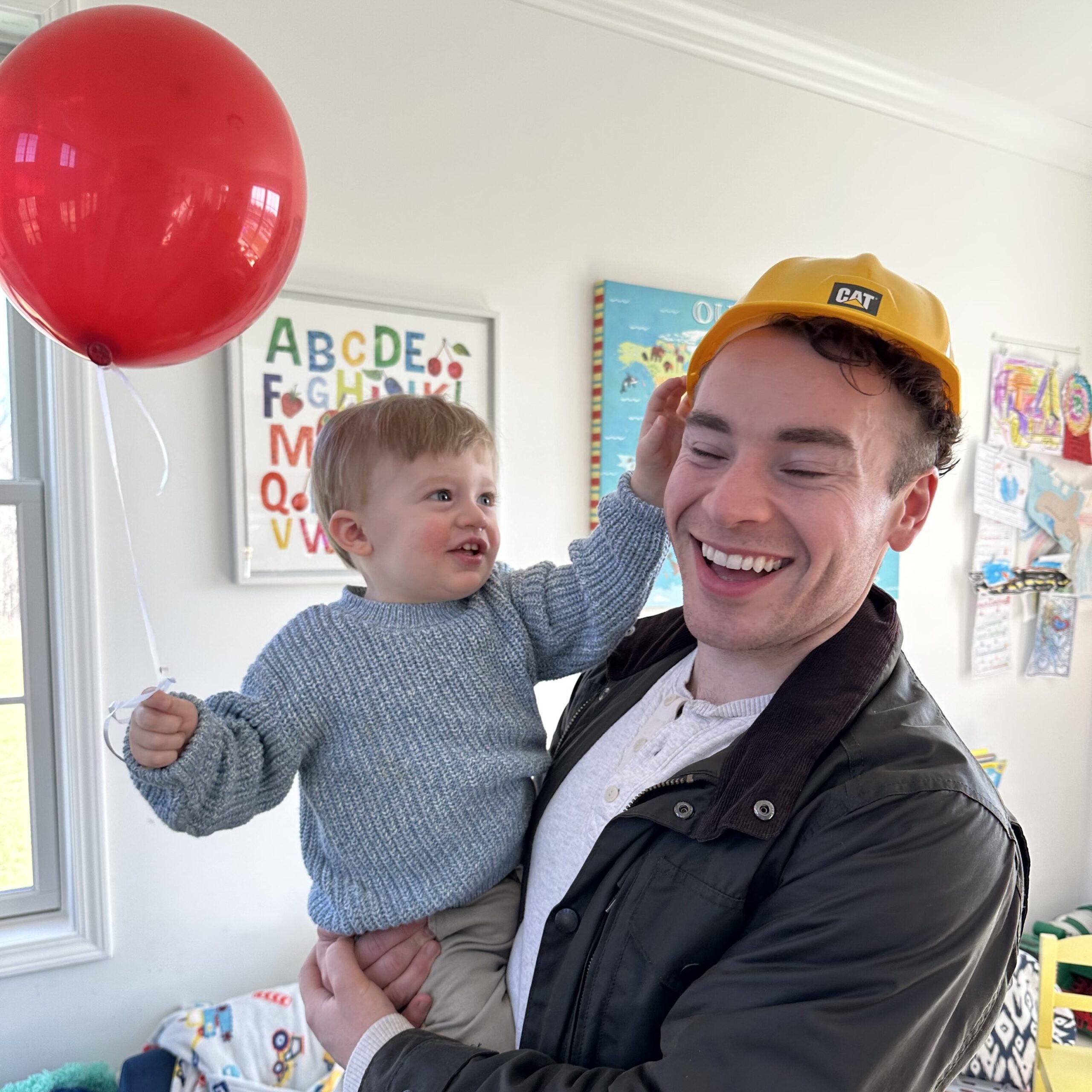 Man and toddler with red balloon and toy CAT construction helmet