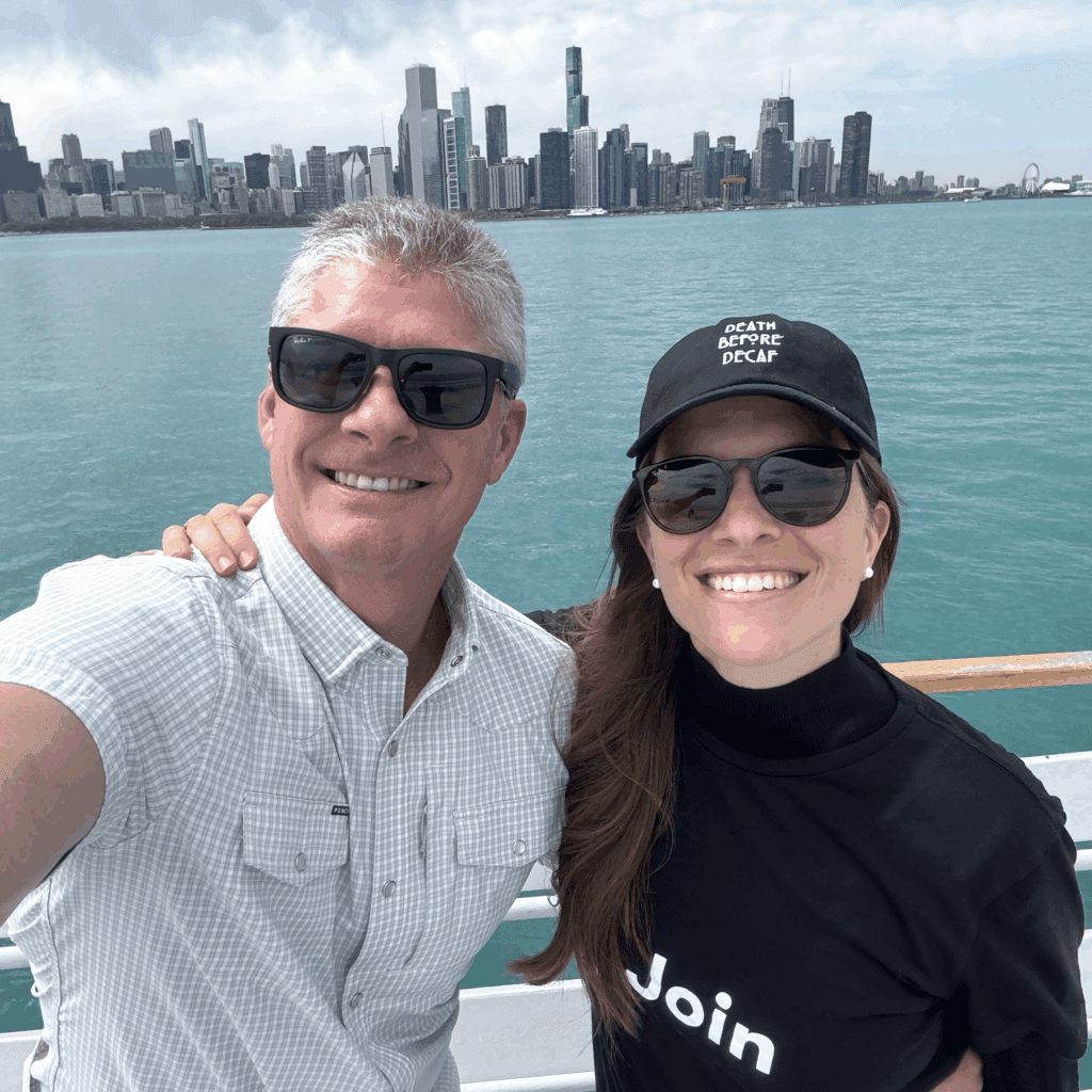 Couple smiling with Chicago skyline backdrop. The woman's hat says "DEATH BEFORE DECAF".