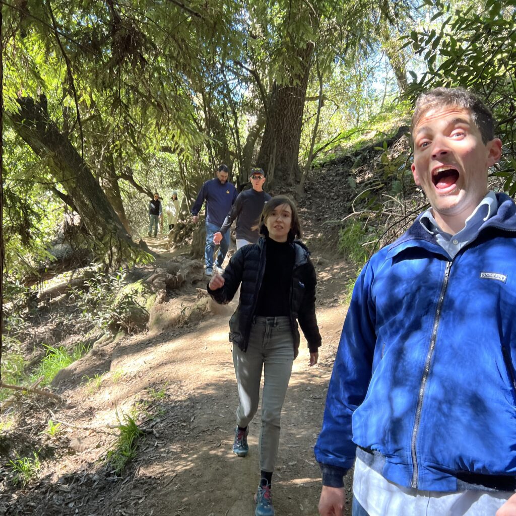 Hikers on a wooded trail, one man with surprised expression in foreground.