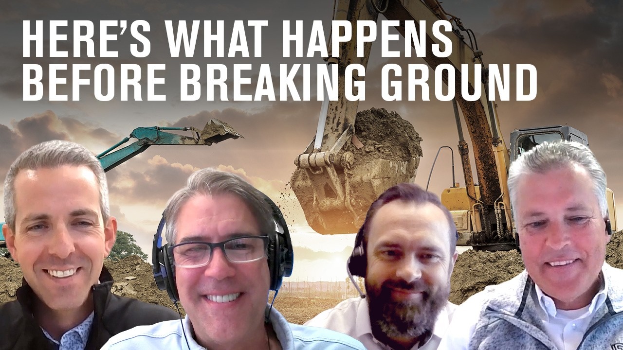 Preconstruction discussion with four men, construction equipment in background. Here's What Happens Before Breaking Ground.